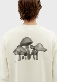 Creme-kleurige sweatshirt met een zwarte afbeelding van drie paddenstoelen op de achterkant, met subtiele schaduwen en details, die verschillende vormen toont.