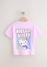 T-shirt rose clair à manches courtes sur un cintre en bois avec le texte coloré « HELLO KITTY » et un chat dessin animé tenant un nœud sur un fond à carreaux.