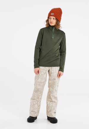 Long-sleeve, olive green top with a half-zip collar, paired with beige pants featuring a subtle white pattern, and black footwear.