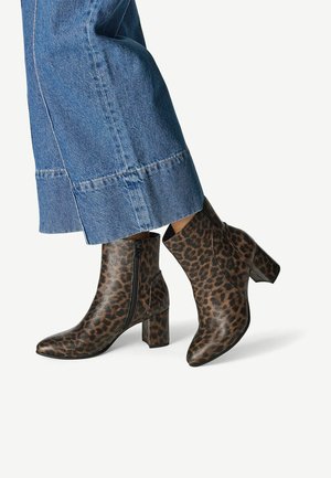 Person trägt blaue Jeans mit weitem Bein und braune, leopardgemusterte Stiefeletten mit Blockabsatz und seitlichen Reißverschlüssen.