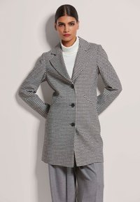 Zwart-wit houndstooth jas met notch-lapels, enkele knoopsluiting en zijzakken, gecombineerd met een witte turtleneck.