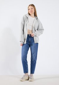 Felpa con zip grigia chiara dal taglio comodo, abbinata a jeans blu a vita alta e sneaker grigie chiare con accenti viola.