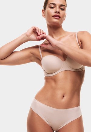 Beige bh en bijpassende slip gemaakt van glad stof. De bh heeft lichte padding en dunne verstelbare bandjes; de slip heeft een naadloos ontwerp.