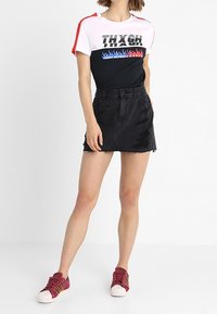 Tričko s krátkým rukávem, v kombinaci barev s červenými akcenty a grafickým textem, doplněné o černou denimovou sukni a vínové tenisky s bílou podrážkou.