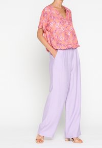 Top a maniche corte, con scollo a V e motivo floreale in corallo e viola, abbinato a pantaloni larghi di un delicato viola, per un silhouette rilassata.