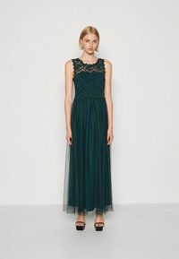 Rochie maxi verde închis cu corset din dantelă, design fără mâneci și fustă din tul. Are talie strâmtă și o siluetă vaporoasă.