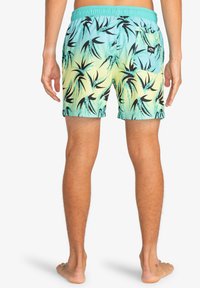 Costumi da bagno realizzati in tessuto leggero, con un gradiente che va dall'acqua al giallo, decorati con motivi di foglie tropicali nere. Vita elastica con tasca posteriore.