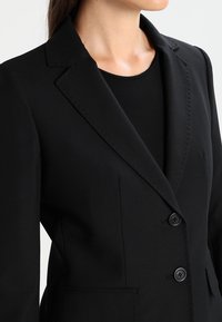 Zwarte blazer van gladde stof, met een getailleerd silhouet, ongelapte revers, twee knopen en zijzakken.