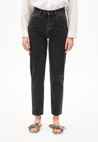 Höga svarta denimjeans med en avsmalnande passform, fem fickor, subtila slitningar och dragkedja, tillsammans med sandaler med grå rosett.