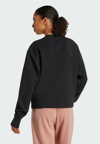 Felpa nera oversize con scollo rotondo, polsini a coste e finitura tessurizzata, indossata su pantaloni rosa chiaro.