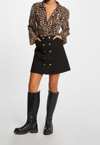 Bluse med leopardprint, lange ærmer og dyb V-hals, parret med en sort A-line nederdel med sølvknapper og lommer. Sorte knæhøje støvler.