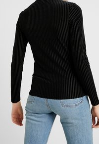 Schwarz langärmeliges Oberteil mit vertikaler Rippstruktur, figurbetontem Design und Rundhalsausschnitt, kombiniert mit hellblauen Jeans.