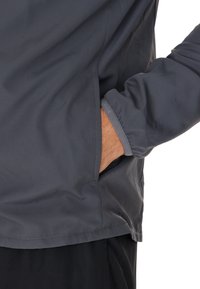 Grå lättviktsjacka med sidficka, slät yta, elastiska manschetter och en minimalistisk design. Skräddarsydd för enkel rörelse.