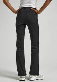 Jeans in denim nero con una vestibilità slim, caratterizzati da due tasche posteriori e una chiusura con zip. Il materiale è liscio con dettagli di cucitura sottili.