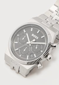 Ασημένιο ρολόι χειρός Hugo Boss με μαύρο καντράν, τρεις υποκαντράν, παράθυρο ημερομηνίας και μπρασελέ από μεταλλικούς κρίκους.