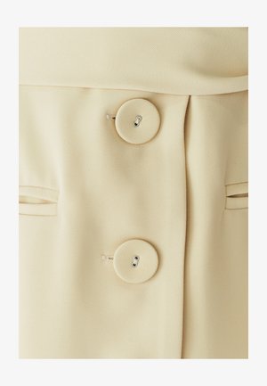 Beige fabric coat buttons with matching fabric-covered buttons and slit pockets on either side.