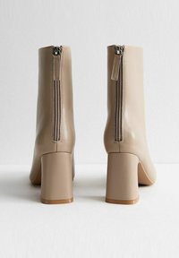 Beige enkellaarsjes met een strakke, glanzende afwerking, voorzien van een opvallende rits aan de achterkant en een chunky hak. Glad textuur en minimalistisch ontwerp.