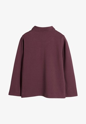 Burgundy színű, hosszú ujjú polo póló galléros nyakkal és lekerekített hátvéggel. Simább, texturált anyagból készült.