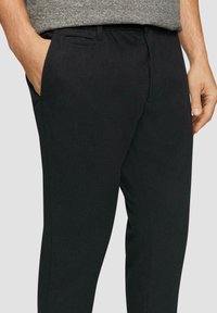 Pantalons noirs en tissu texturé, silhouette slim fit, poches latérales et taille élastique pour le confort.