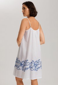 Vestido blanco sin mangas con bordado de hojas azules a lo largo del dobladillo, hecho de un tejido ligero, con finas tirantes ajustables y un corte holgado.
