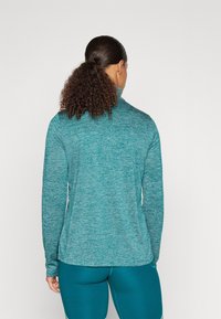 Långärmad träningströja i teal, tillverkad av strukturerad, fukttransporterande tyg. Har en hög krage och en figurnära design med minimala sömmar.