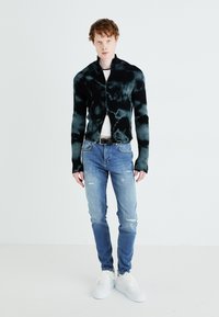 Svart och teal ruggad cardigan med hög krage, ihop med slitna ljusblå jeans och vita sneakers. Enkelt mönster, figurnära passform.