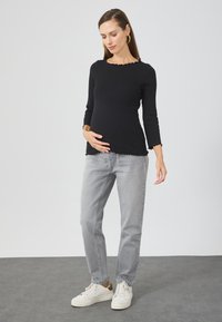 Black ribbed long-sleeve top with a scalloped hem, paired with gray straight-leg jeans and white sneakers. Simple and minimalistic design.