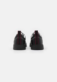 Svarte lær sneakers med teksturert overflate, med røde detaljer på hælen og hvite skolisser, med flat gummisåle.