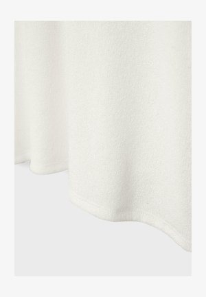 Witte textuurstof met een zichtbare zoom aan de onderkant, zacht vallend tegen een effen lichte achtergrond.