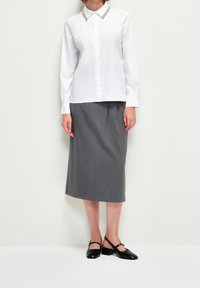 Camicia bianca a maniche lunghe con colletto a punta e gonna a matita grigia, abbinata a scarpe slingback nere. Tessuto liscio e vestibilità sartoriale.