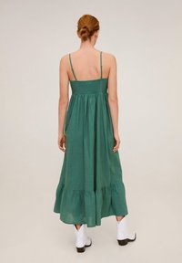Maxi šaty z zelené bavlny s tenkými ramínky, nařaseným živůtkem a volánkovým lemem. Mají volný střih a hladkou teksturu.
