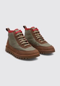 Zapatillas altas casuales en verde oliva y marrón con detalles en rojo, cordones beige y suelas marrones con buen agarre, mostradas en pareja sobre un fondo gris.