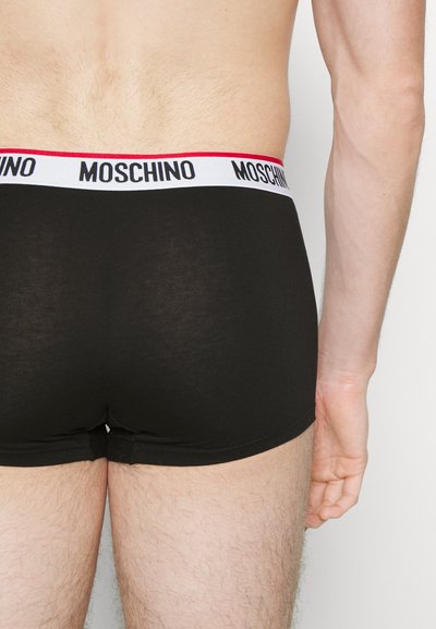 Svarte boxer-shorts med en hvit kant som har "Moschino" i svart tekst og en rød aksent. Stoffet ser glatt ut med en tettsittende design.