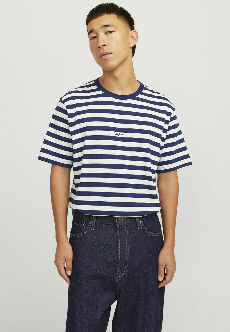 Marineblå og hvid stribet kortærmet T-shirt med rund hals og lille logo centreret på brystet. Sammen med mørke denimbukser.