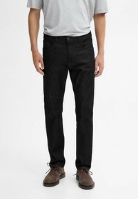 Jeans in denim nero a taglio slim, con classico design a cinque tasche, texture sottile e chiusura con bottoni, abbinati a scarpe in camoscio marrone.