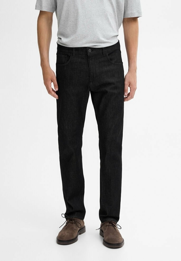 Jeans in denim nero a taglio slim, con classico design a cinque tasche, texture sottile e chiusura con bottoni, abbinati a scarpe in camoscio marrone.