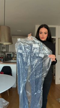 Plave hlače s uzorkom zapakirane u prozirnu plastiku, s oznakama. Tekstura izgleda glatka i blago rastezljiva. U pozadini se vidi kuhinja.