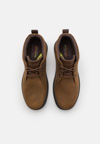 Zapatos de cuero marrón hasta el tobillo con puntera redonda, cordones y un collar acolchado. Presentan plantillas texturizadas y una suela de goma negra contrastante.