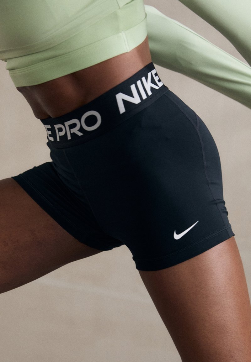 Czarne szorty sportowe z szerokim czarno-białym pasem w talii z napisem "NIKE PRO", z małym białym logo Nike Swoosh w dolnym prawym rogu.