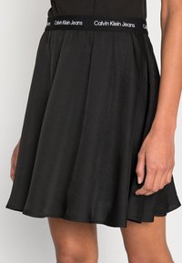 Svart kjol med utsvängd design, tillverkad av ett mjukt tyg. Har en elastisk midja med "Calvin Klein Jeans"-logotyp.
