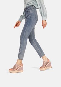Jeans fitted blu chiaro con dettagli strappati e perle decorative sull'orlo. Abbinati a sandali con zeppa lavanda con design a ritagli.