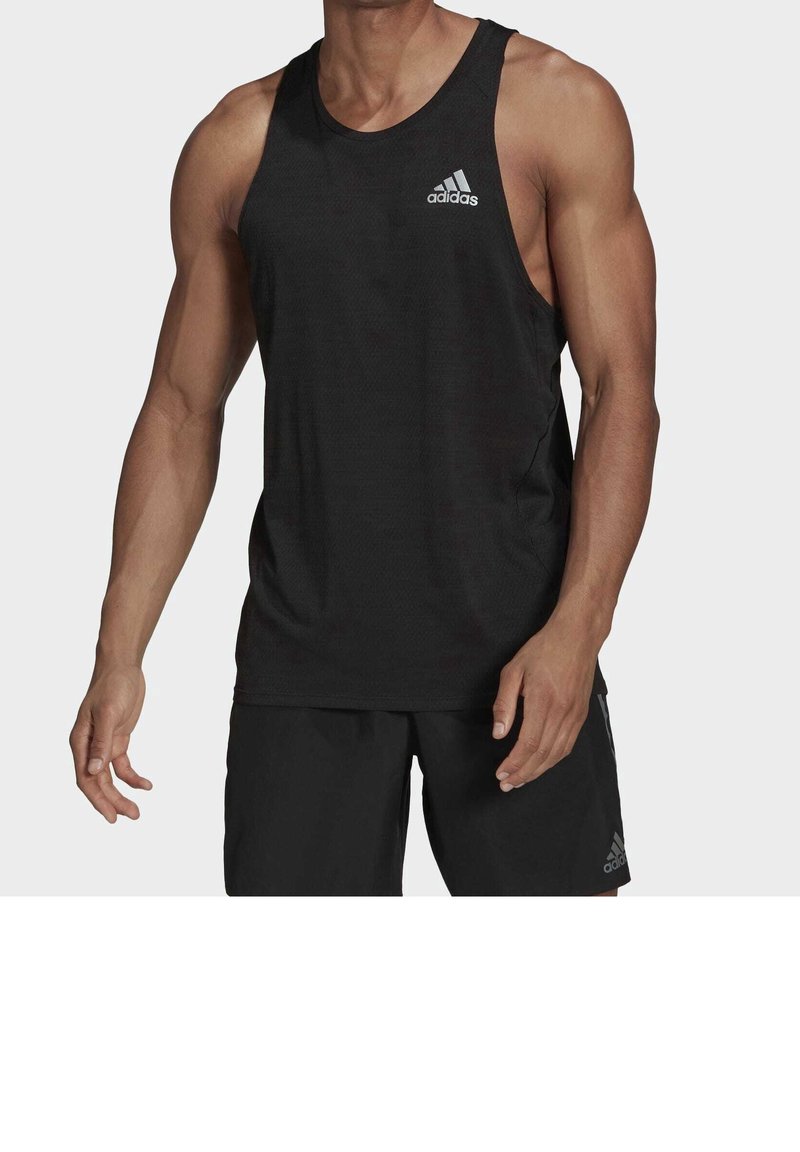 Homme portant un débardeur de sport noir Adidas sans manches et un short noir, debout avec les bras détendus le long du corps.