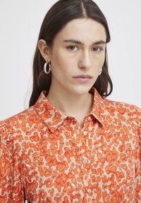 Blusa a maniche puff in stampa floreale arancione, con collo a camicia, chiusura con bottoni e tessuto leggero.