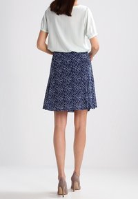 Light green short-sleeve top paired with a navy flared skirt featuring a small floral pattern and a textured fabric. Beige high-heeled shoes.