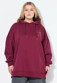 Felpa oversize bordeaux con cappuccio e coulisse, caratterizzata da un semplice motivo a fiocco rosa chiaro sul petto e polsini e orlo a costine.
