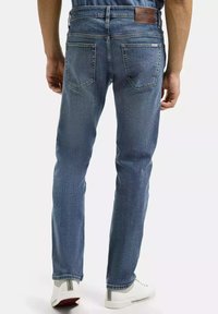 Niebieskie dżinsy typu straight fit z skórzaną łatą na pasku i dwoma tylnymi kieszeniami. Noszone z białymi trampkami.