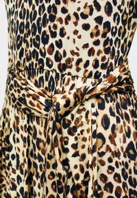 Φόρεμα με λεοπάρ μοτίβο σε ελαφρύ ύφασμα, με λεπτομέρεια δεμένη στη μέση, σε αποχρώσεις καφέ και μαύρου σε κρεμ φόντο.