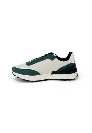 Zapatillas con una parte superior de malla beige y acentos de ante verde oscuro, suela de goma negra y un diseño elegante y aerodinámico.