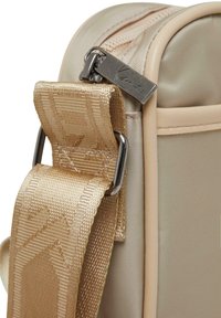 Borsa a tracolla color tan con una finitura satinata liscia, tracolla regolabile e testurizzata, cerniera in metallo e etichetta con marchio. Presenta una forma rettangolare strutturata.