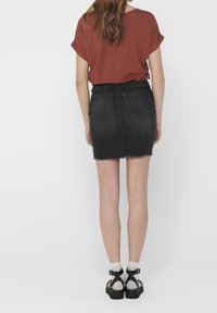 Czarna dżinsowa mini spódnica z postrzępionym dołem, dwoma tylnymi kieszeniami i wysokim stanem, zestawiona z rudym t-shirtem z krótkim rękawem i czarnymi sandałami.